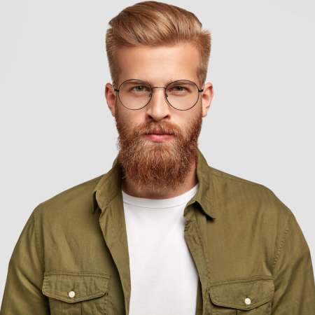 serious-unshaven-man-with-ginger-hair-beard-looks-directly-thinks-about-something-wears-fashionable-shirt-round-spectacles-isolated-white-wall-masculinity-concept